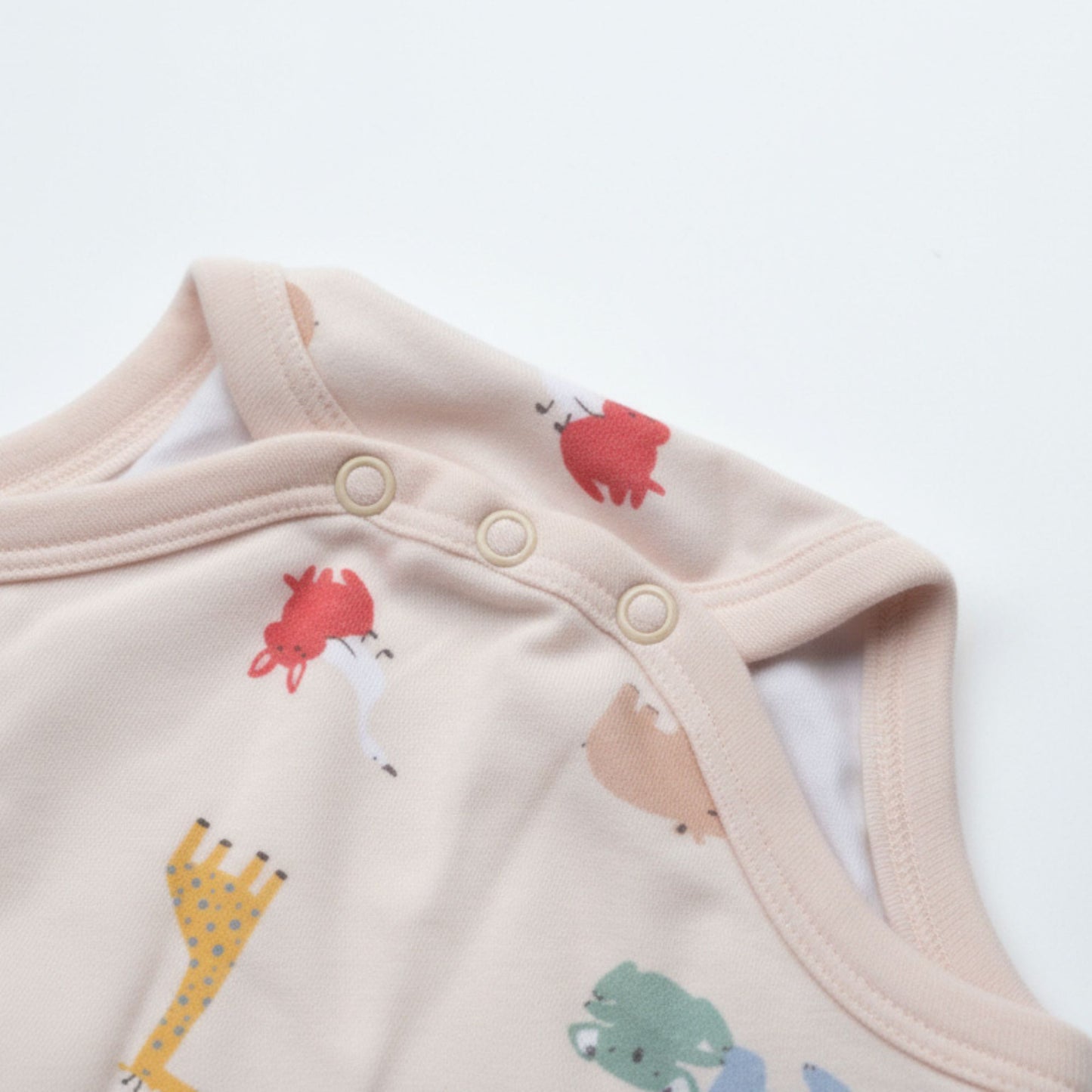 Detaljbild av ekologisk babybody från kollektionen Safari Vänner med knappar på axeln och djurmönster på rosa botten