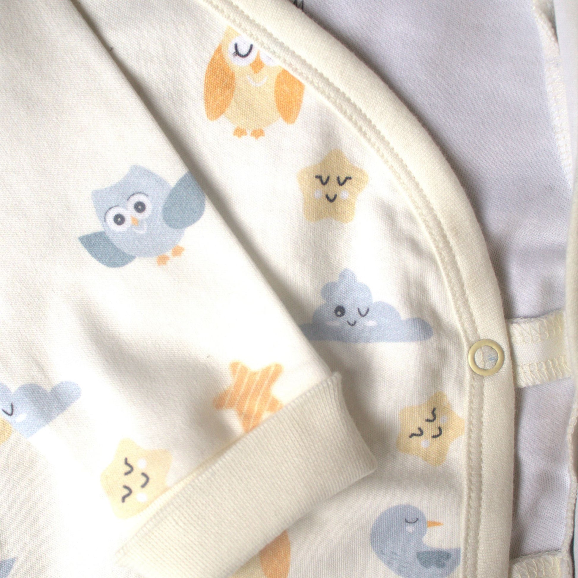 Detaljbild av ekologisk omlott-body från kollektionen Himlens Vänner med kantband och tryckknappar samt fågel-, moln- och stjärnmönster