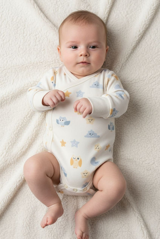 Baby som bär ekologisk omlott-body från kollektionen Himlens Vänner med fågel- och stjärnmönster, liggande på filtdyna