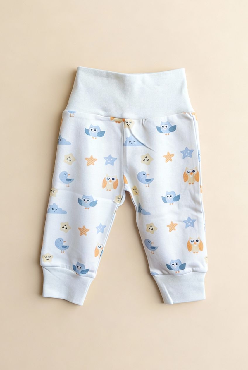 Ekologiska babybyxor från kollektionen Himlens Vänner med fågelmönster, flatlay på beige bakgrund