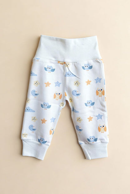 Ekologiska babybyxor från kollektionen Himlens Vänner med fågelmönster, flatlay på beige bakgrund