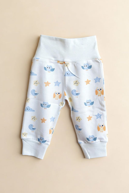 Ekologiska babybyxor från kollektionen Himlens Vänner med fågelmönster, flatlay på beige bakgrund