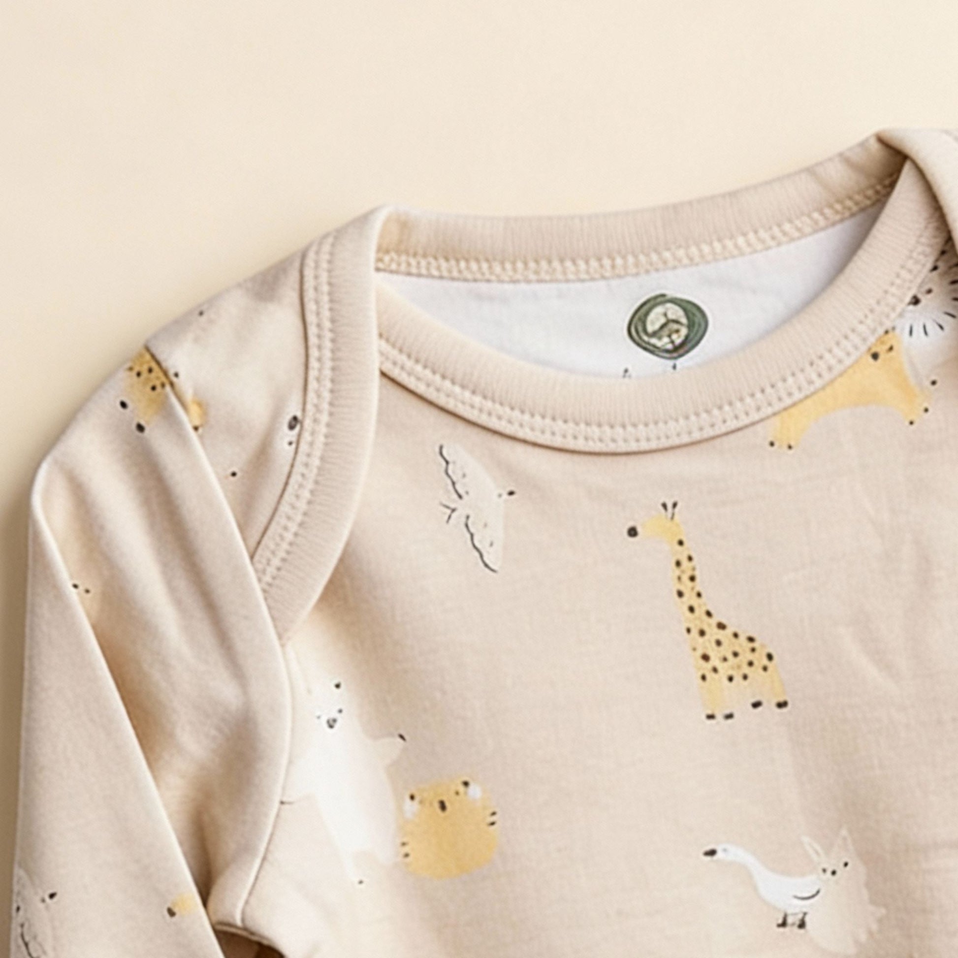 Detaljbild av ekologisk babybody från kollektionen Safari Vänner med halsringning och djurmönster i beige toner