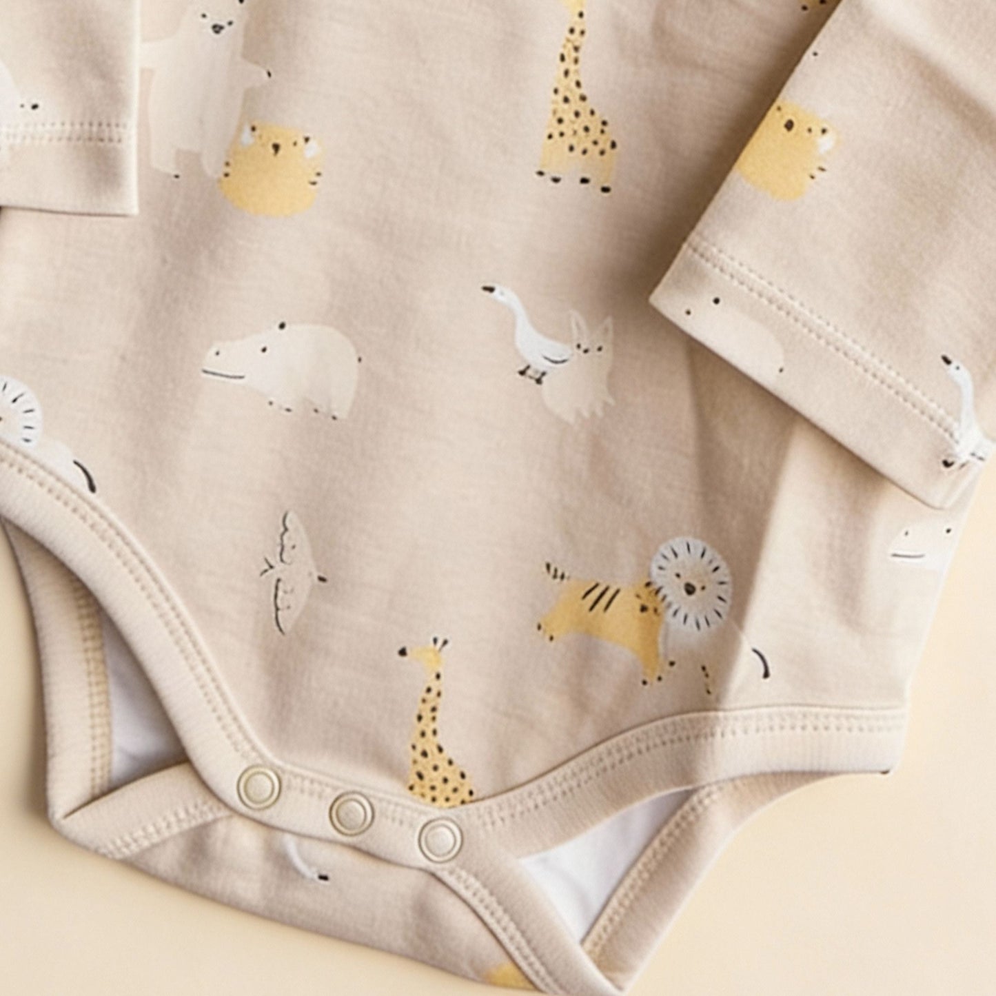 Detaljbild av ekologisk babybody från kollektionen Safari Vänner med knappar i grenen och djurmönster i beige toner