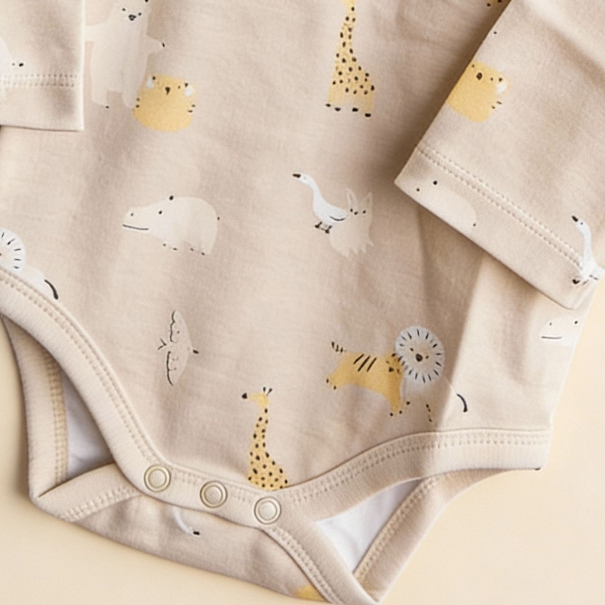Detaljbild av ekologisk babybody från kollektionen Safari Vänner med knappar i grenen och djurmönster i beige toner