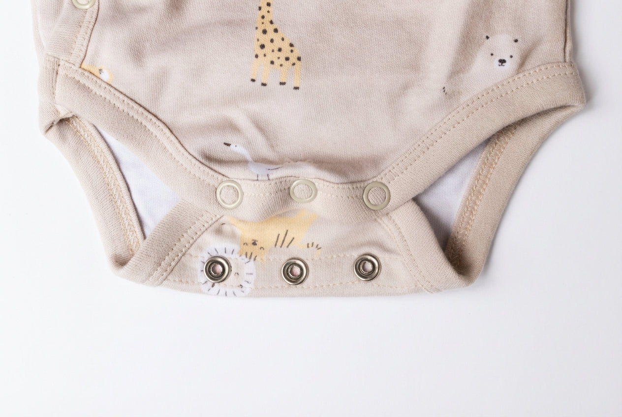 Detaljbild av ekologisk omlottbody från kollektionen Safari Vänner med knappar i grenen och djurmönster i beige toner