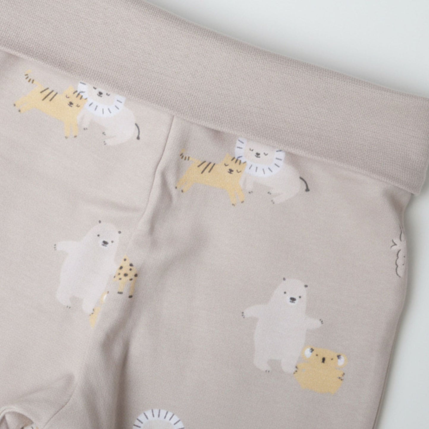 Detaljbild av ekologiska babybyxor från kollektionen Safari Vänner med mjuk midja och djurmönster i beige toner