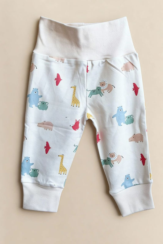 Ekologiska babybyxor från kollektionen Safari Vänner med färgglatt djurmönster på vit botten, flatlay på beige bakgrund